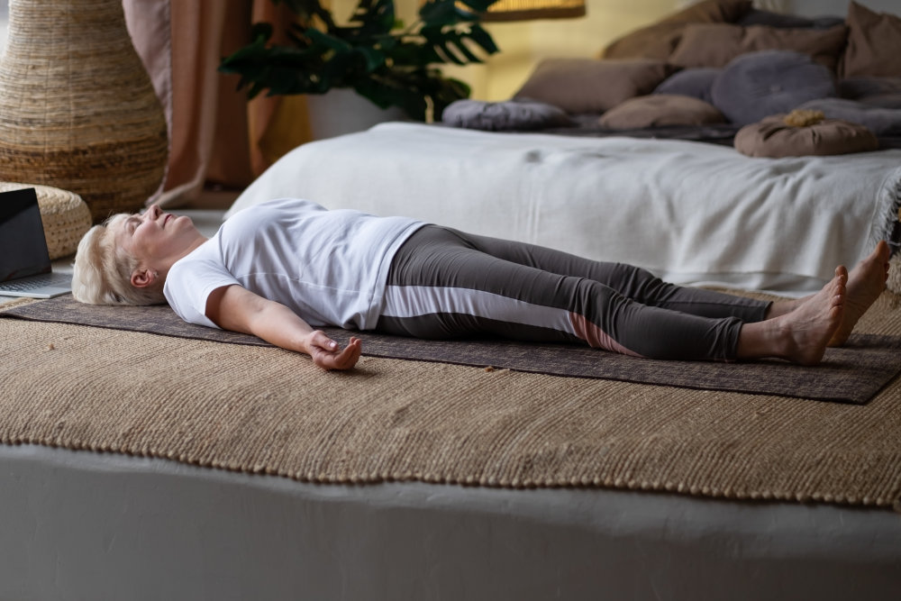 Senior woman lying in savasana, practicing therapeutic yoga nidra at home