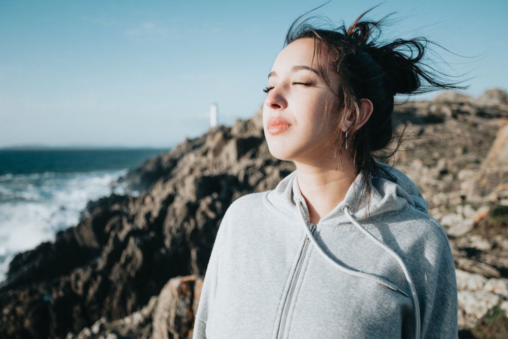 Young woman practicing breathwork outside near a lighthouse to prevent a panic attack.