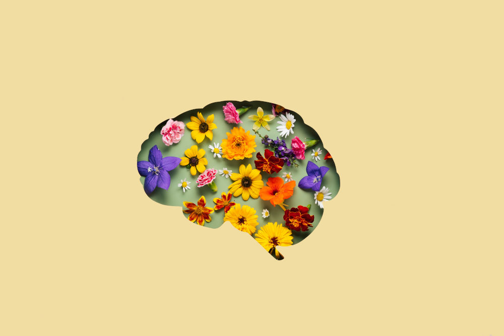 Paper cut brain and flowers on yellow background, evoking the complexity and beauty of neuroscience and meditation for mental health.