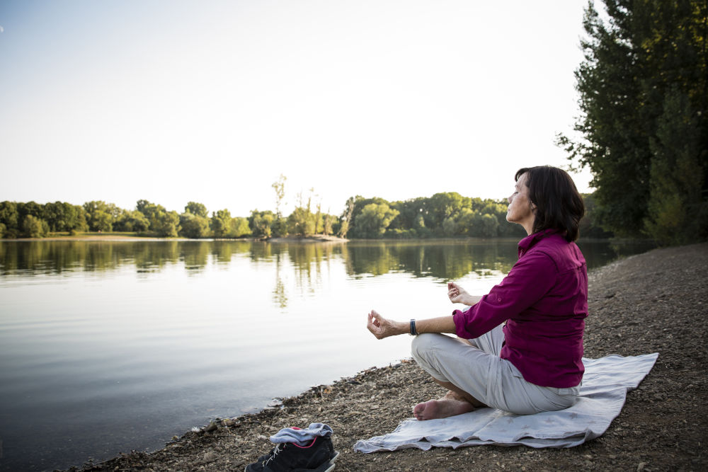 Senior woman at a lake practicing meditation for mental health